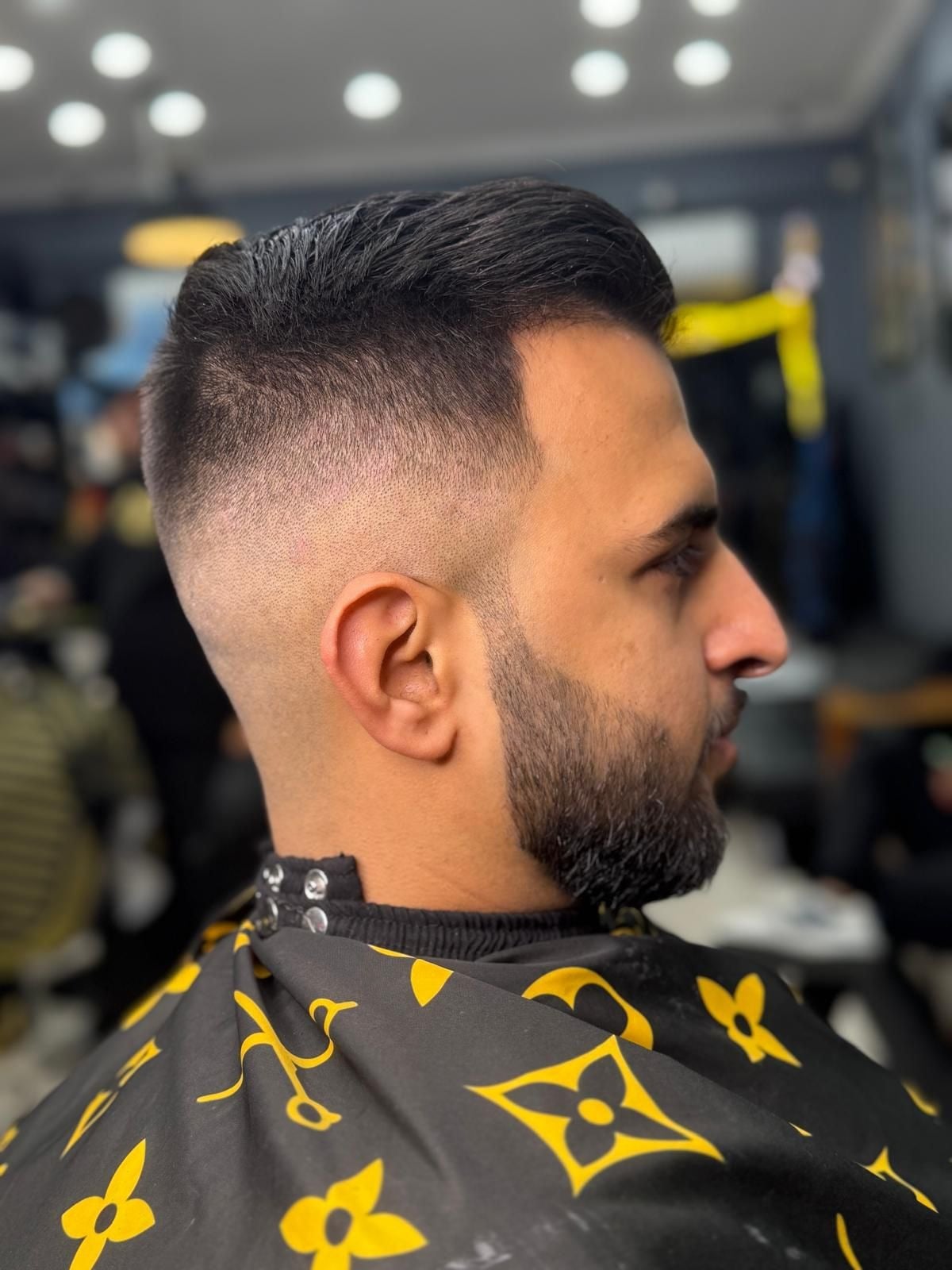 Side profile pompadour with a skin fade and beard in a bright shop