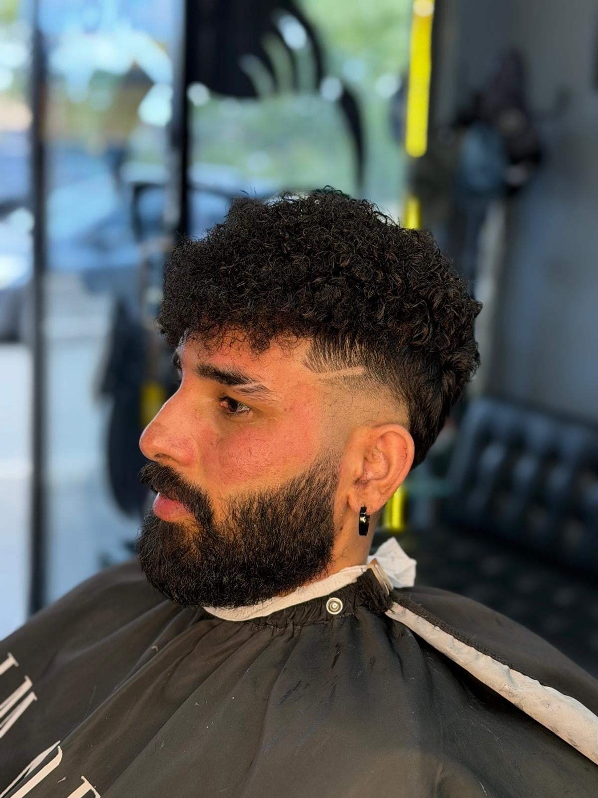 Curly top taper fade with a shaved neck design, side profile in the chair